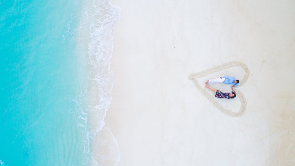 man and woman lying on white sand near sea shore